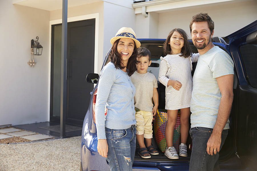 Personal Insurance - Portrait of Family Standing in Front of Their Home and Packing Their Car to Get Ready For a Summer Vacation